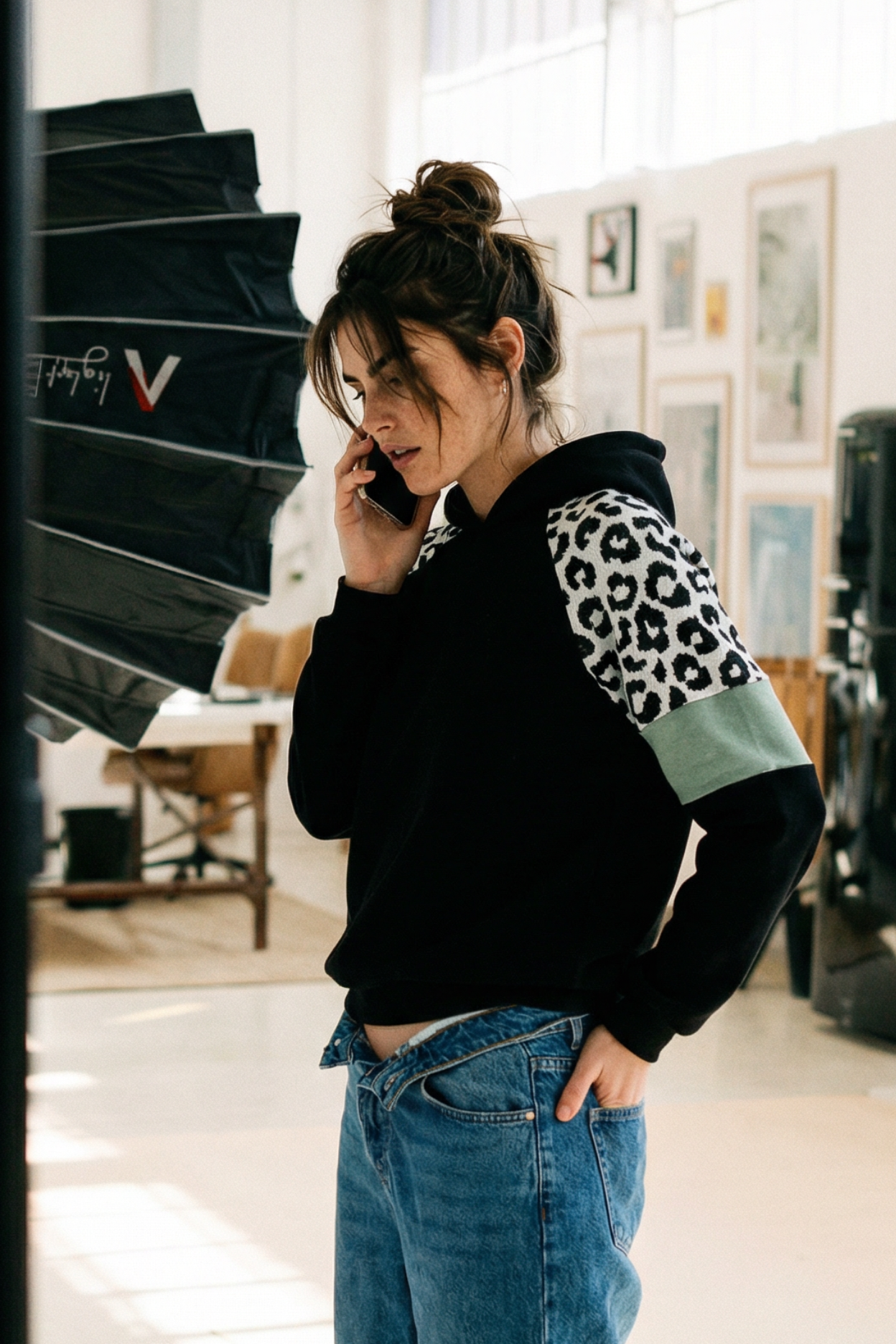 Woman talking on a phone wearing a black hoodie with colorful sleeves in an indoor setting.