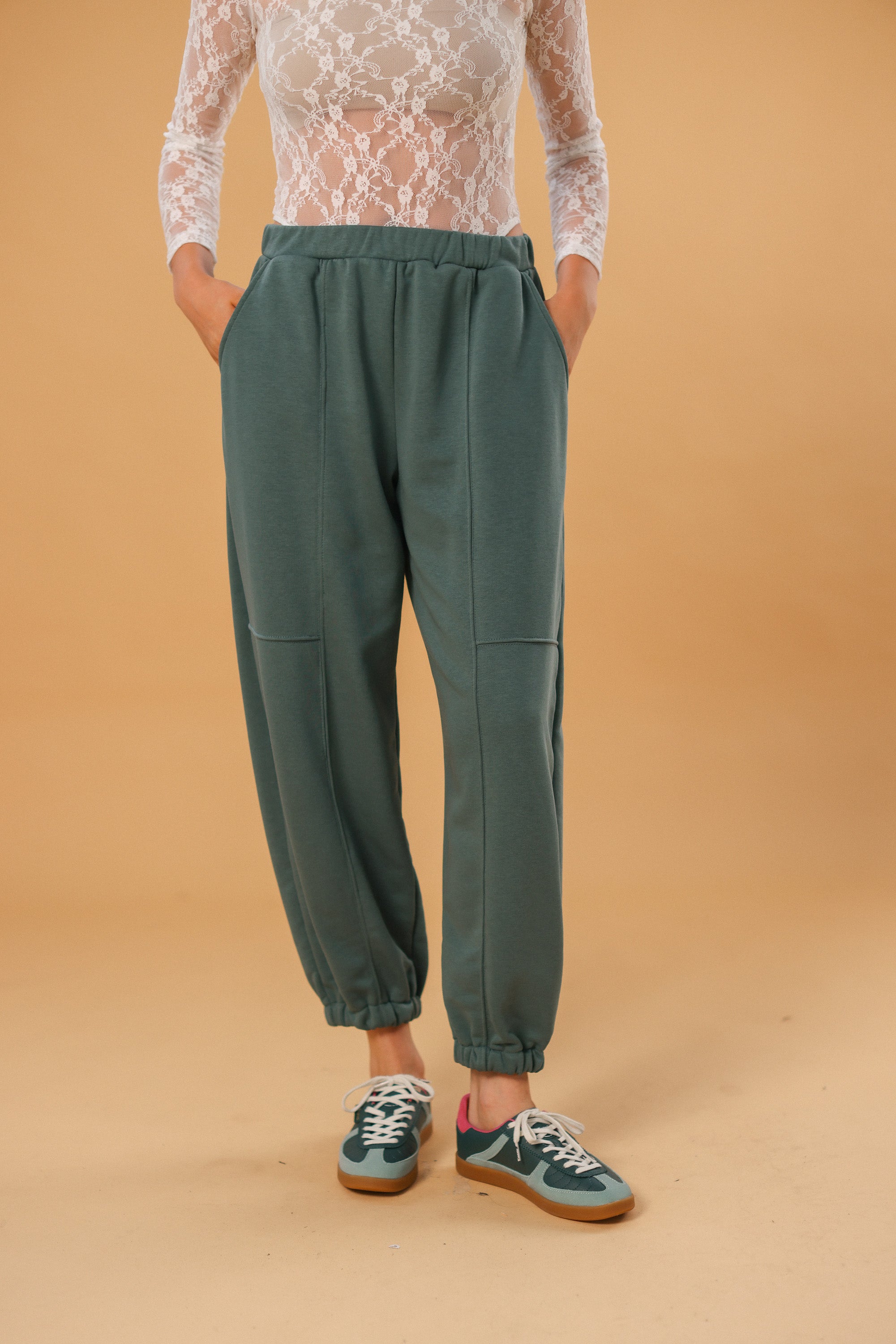 Person wearing green pants and a lace top on a beige background