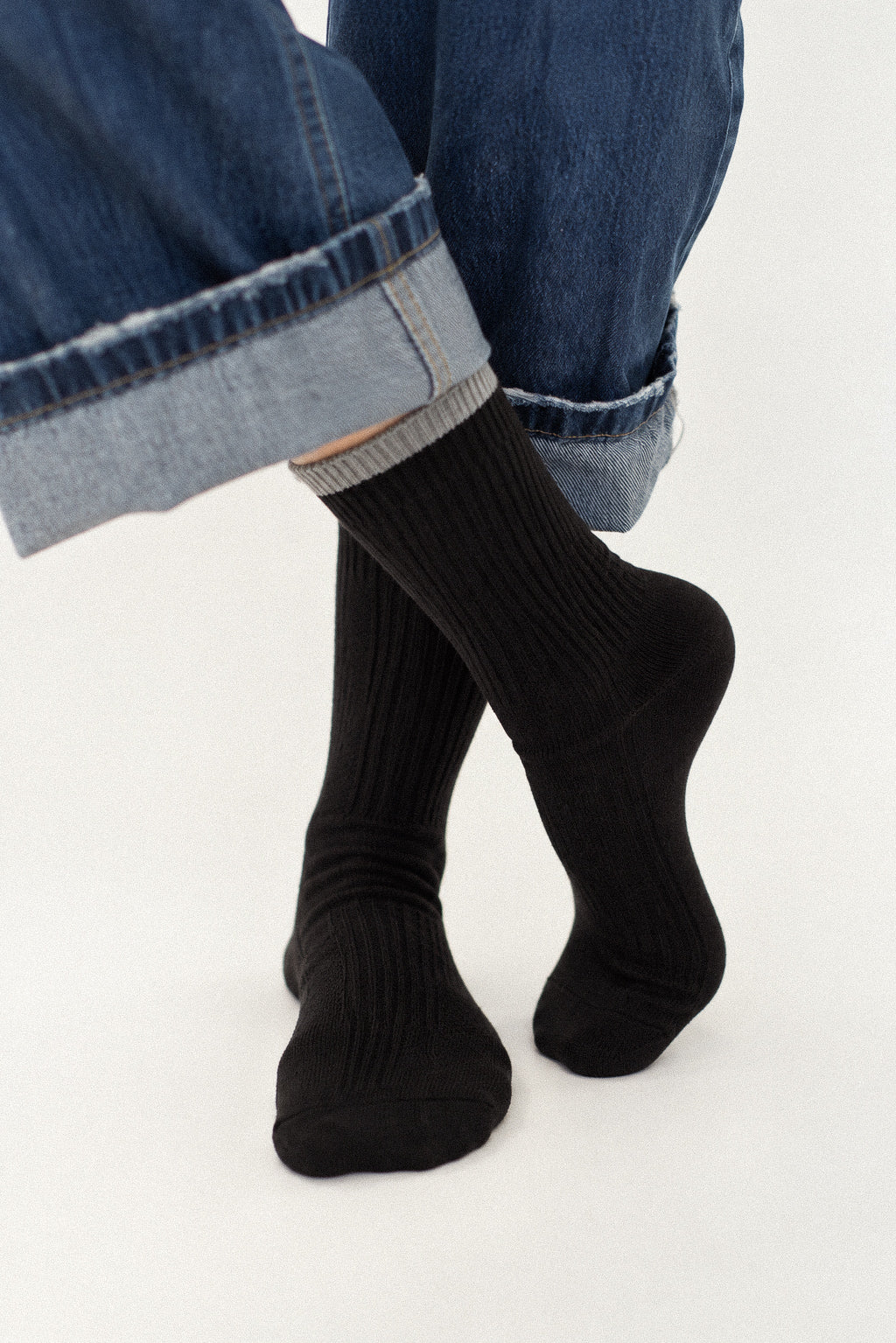 Black ribbed crew socks worn with cuffed blue jeans on a person's feet, shown against a plain white studio background.