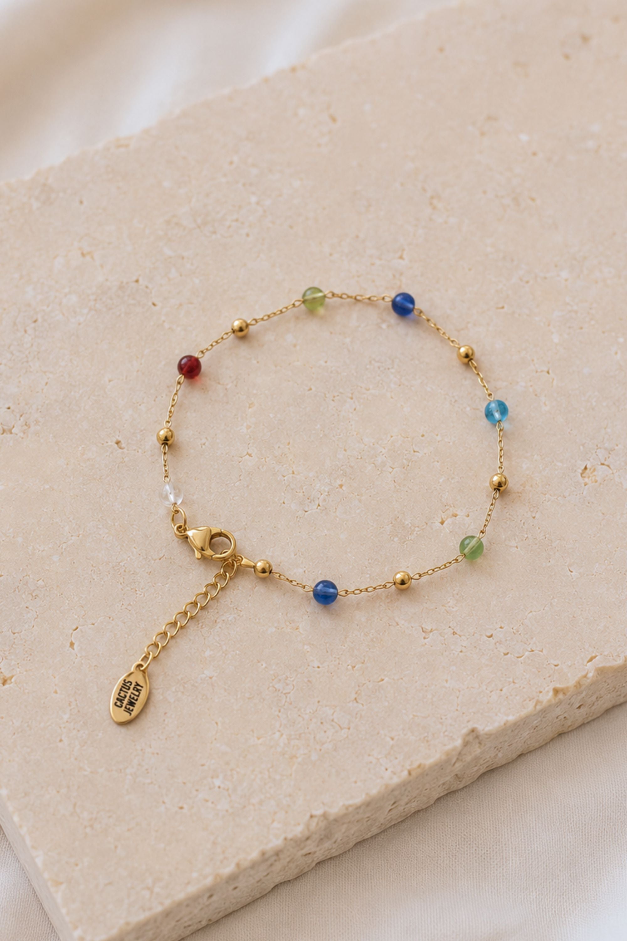 Gold bracelet with colorful beads on a beige stone surface