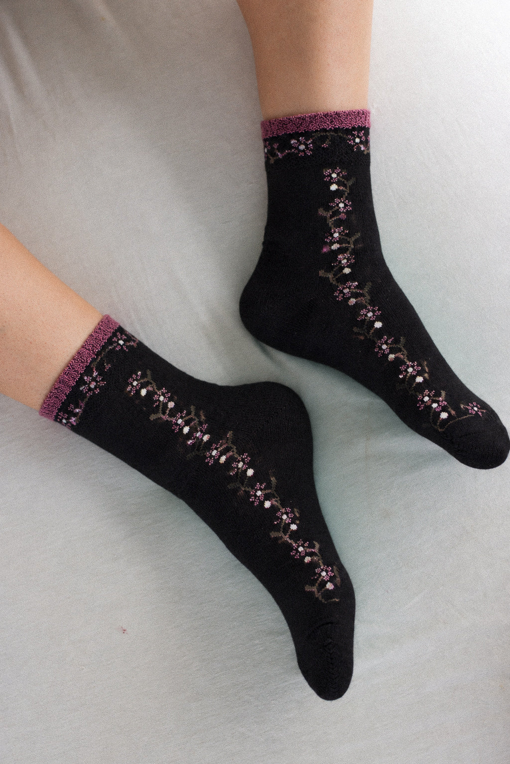Black crew socks with purple floral lace trim and a textured purple cuff, shown worn on feet against a light gray background.
