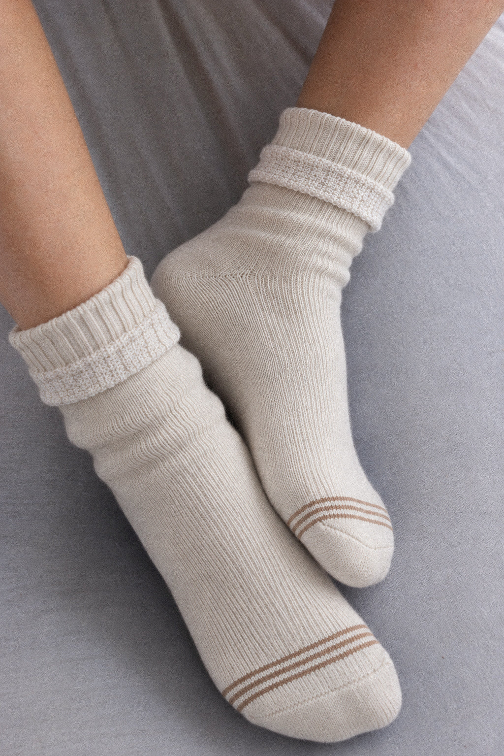 A pair of off-white crew socks with brown stripes near the toes, worn on feet resting on a gray fabric surface.