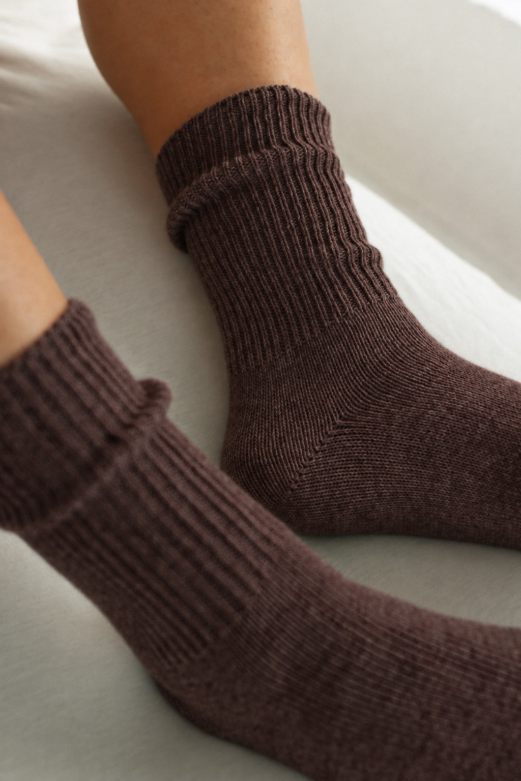 A close-up of a person's feet wearing dark brown ribbed knit crew socks on a light-colored surface.