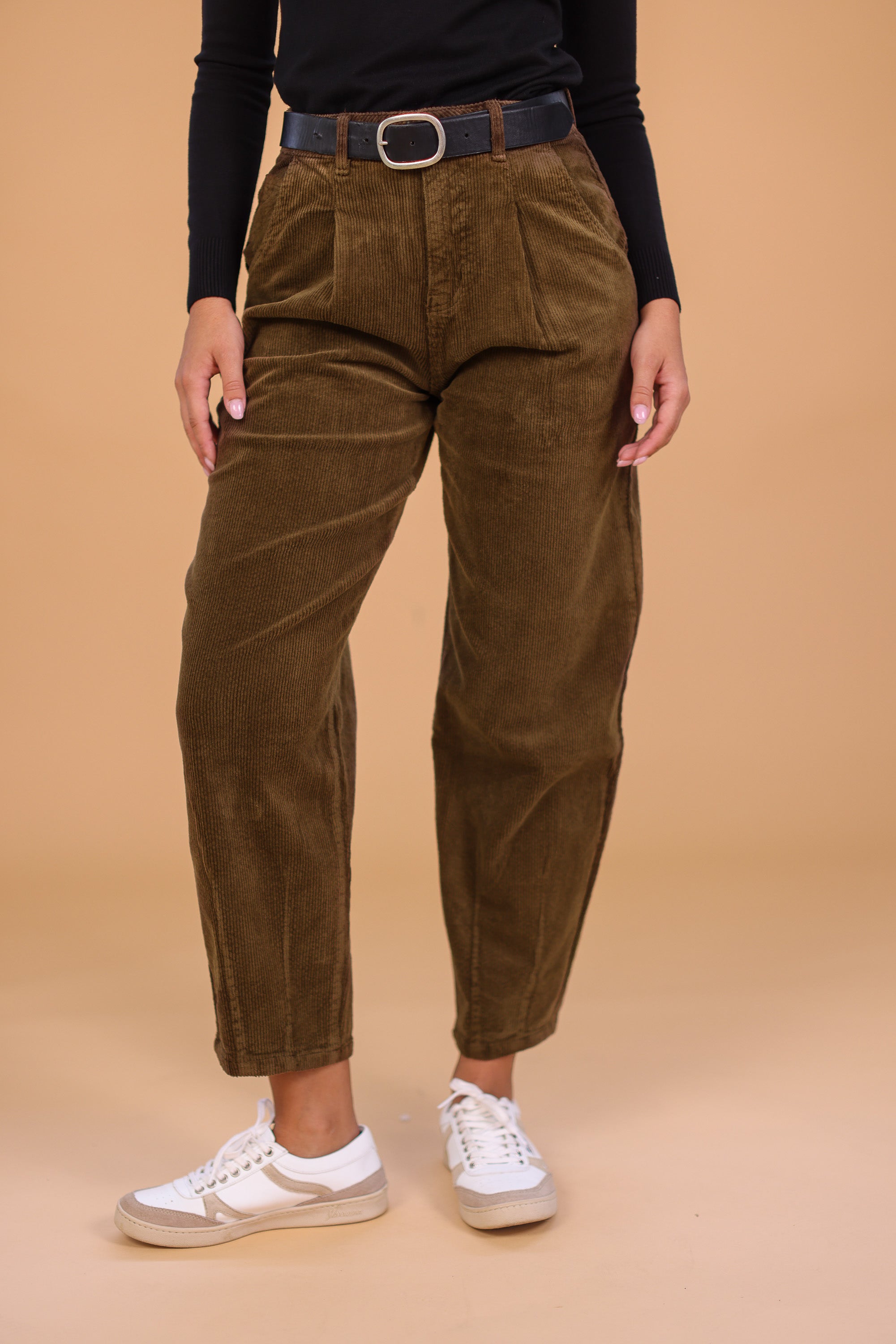 woman wearing khaki corduroy pants with a black belt and white sneakers 